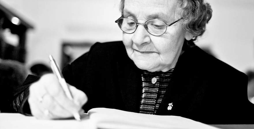 older lady writing with a pen in a notebook in black and white image