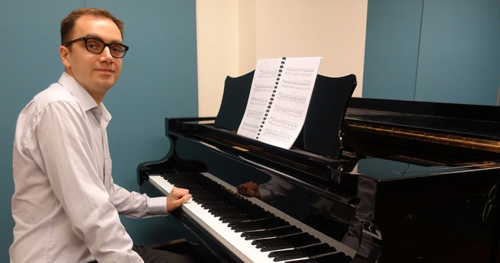 Composer Cyrus Meurant sitting down at a piano