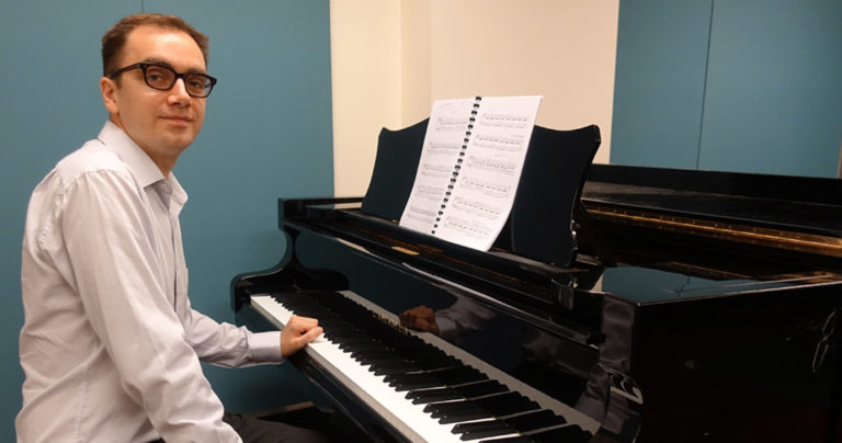 Composer Cyrus Meurant sitting down at a piano